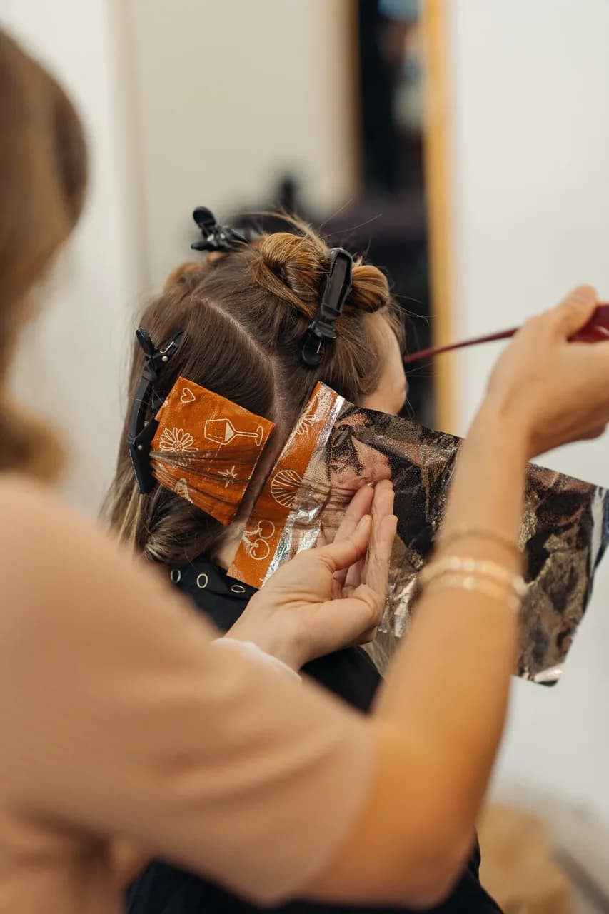 A stylist lifting a section of hair with a tail comb above colour foils