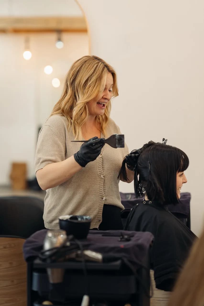 A stylist applying hair colour to a client’s short dark bob