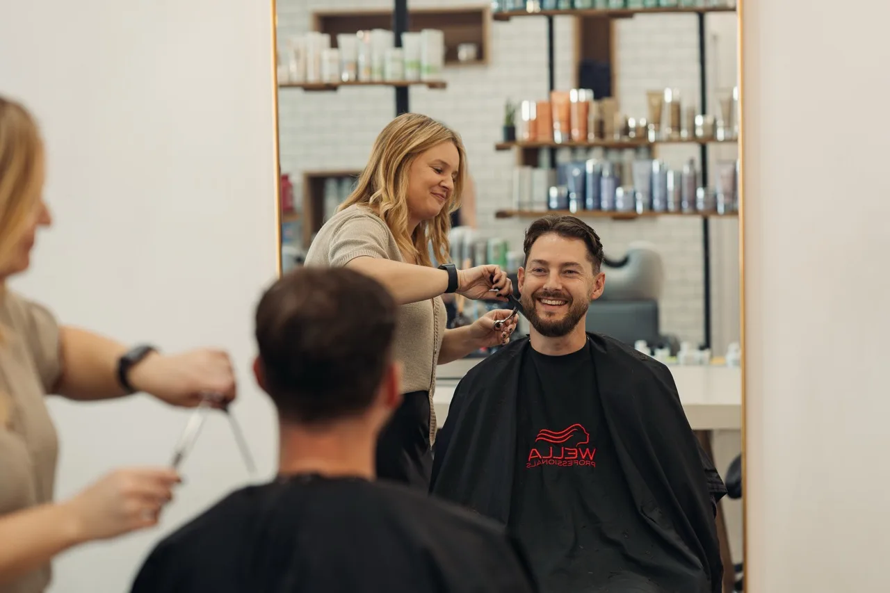 A stylist cutting a smiling man’s hair in a salon