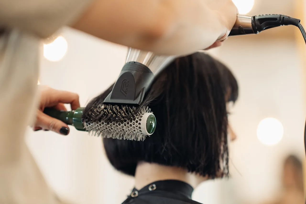 A stylist blow-drying a short dark bob with a round brush