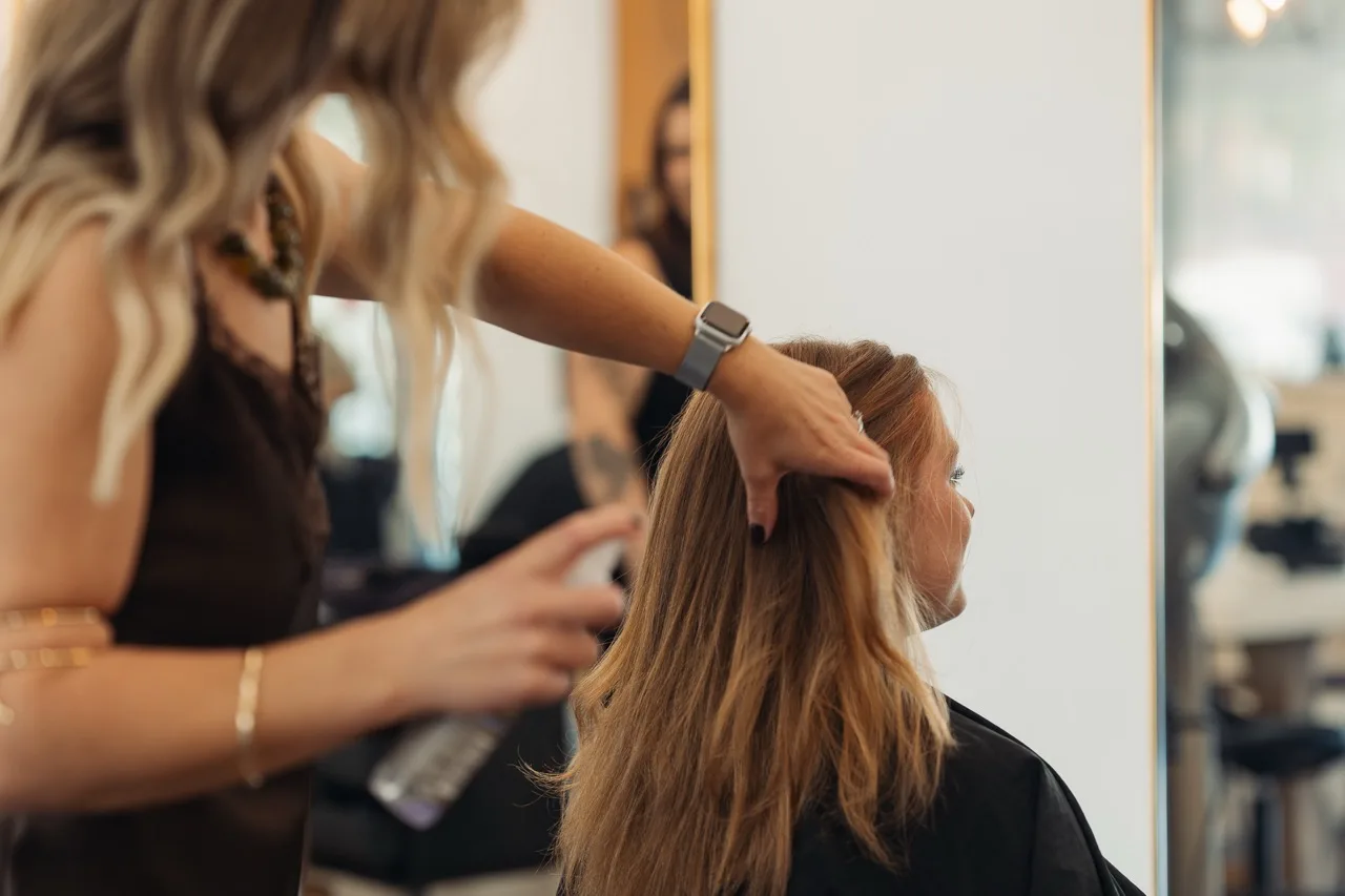 A stylist arranging a seated client’s long hair in a salon